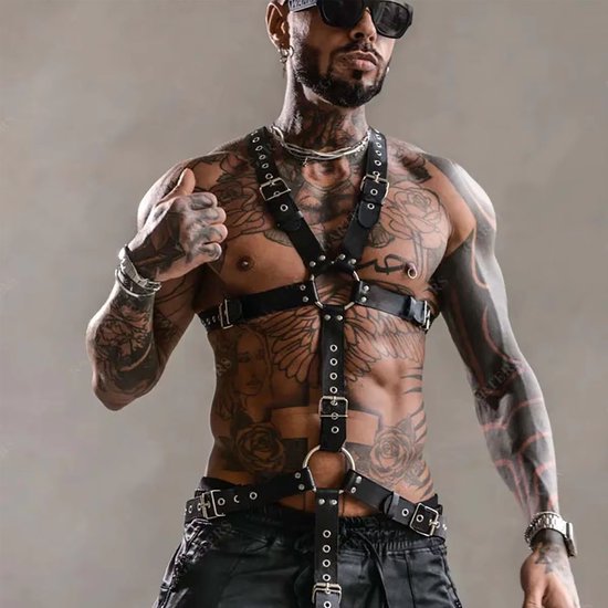 Man met een zwart kunstleren harnas met gespen en ringen, tattoos, zonnebril en leren broek.