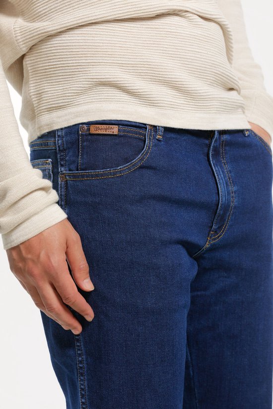 Dichtbij opname van een spijkerblauwe Wrangler spijkerbroek met bruine naden en een bruin leren label op de zak.
