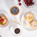 Twee gebakjes, een taartje met blauwe bessen, een fruittaartje en een kopje koffie op een marmeren ondergrond.