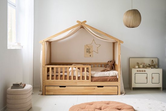 Maisonnette en bois 'Maison' avec ciel de lit en lin, barrières, tiroirs et un lit avec un ours en peluche, dans une chambre d'enfant.