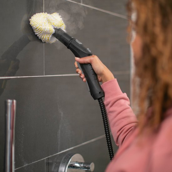 Femme nettoyant un mur carrelé gris foncé avec le nettoyeur vapeur.