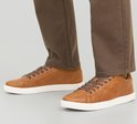 Model draagt bruine leren Jack & Jones sneakers met witte zolen en bruine broek.