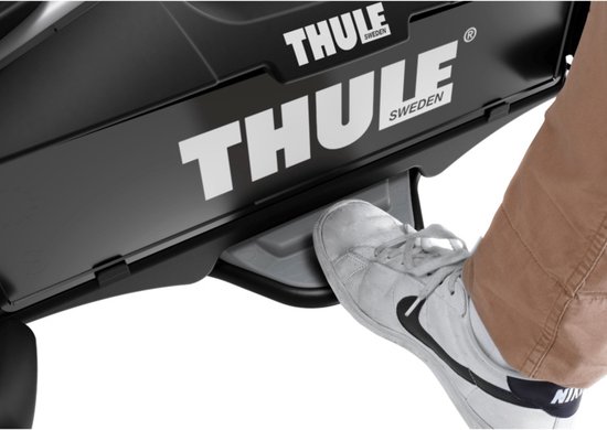 Voet die op de ontgrendelingshendel van de Thule fietsendrager drukt.