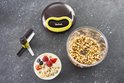 Een Tefal hakmolen met een bakje gehakte walnoten, een komje met yoghurt en fruit, en de losse mesjes.