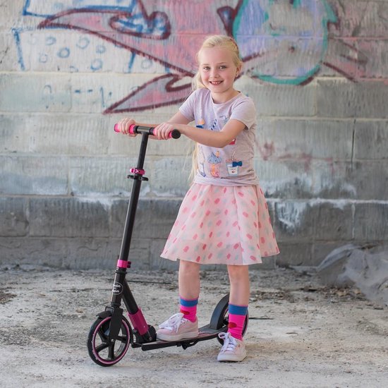 Lachend meisje met blonde staartjes, roze rokje met stippen, staat op zwarte step met roze details.