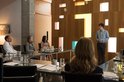 Groep mensen aan een vergadertafel met een man die een presentatie geeft, drie luisteraars en een persoon van achteren gezien.