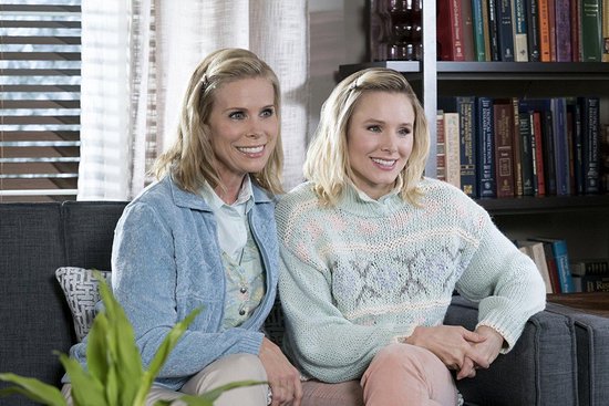 Twee vrouwen zitten op een bank, één met blond haar draagt een gebreide trui.