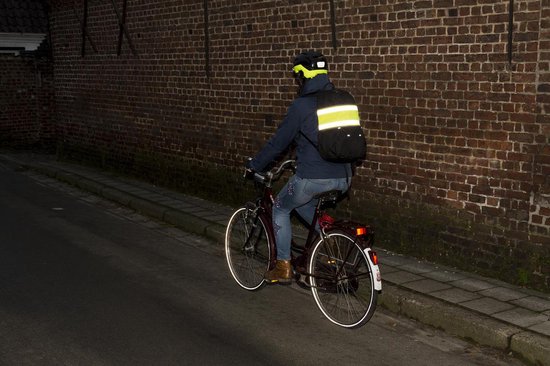 Persoon op fiets met helm en rugzak, draagt reflecterende kleding en fietsband.