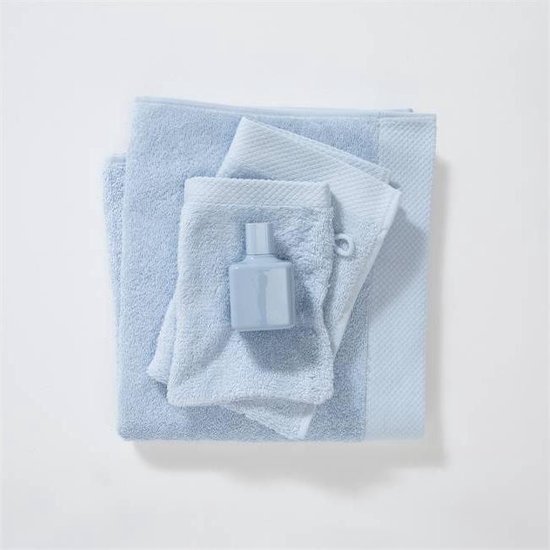 Een set lichtblauwe handdoeken van verschillende maten, met een klein blauw flesje.