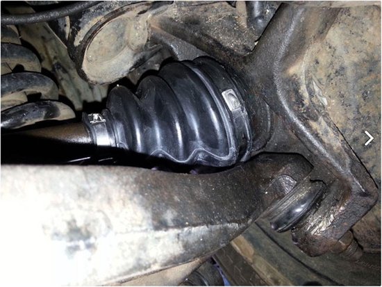 Zwarte rubberen beschermhoes met ribbels, gemonteerd op een auto-as bij de ophanging en de fuseekogel.