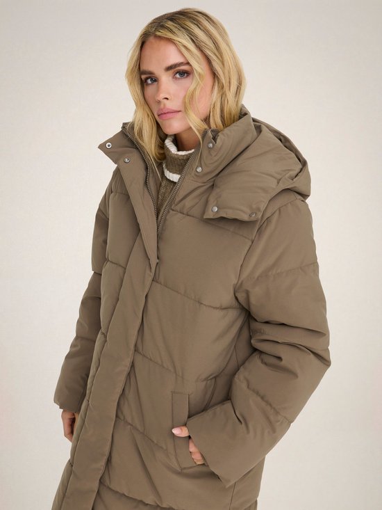 Een vrouw met blond haar draagt een lange, bruine pufferjas met capuchon.