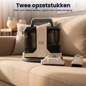Een witte en zwarte vlekkenreiniger met twee opzetstukken op een stoffen bank.