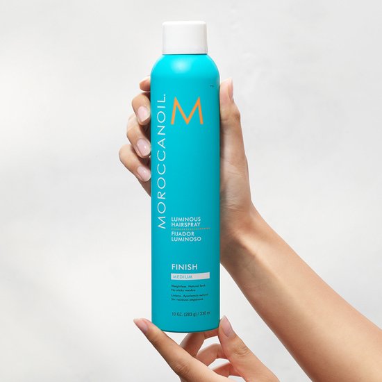 Hand met Moroccanoil Luminous Hairspray Medium, turkooizen spuitbus met oranje M-logo. 330 ml.