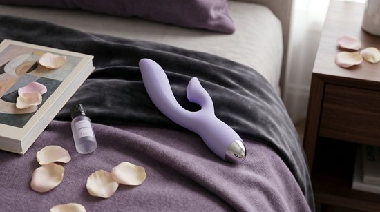 Paarse vibrator op een bed met paarse en grijze dekens, naast een boek en rozenblaadjes.