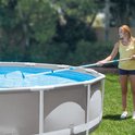 Een blonde vrouw in geel T-shirt gebruikt een schepnet om een zwembad schoon te maken.