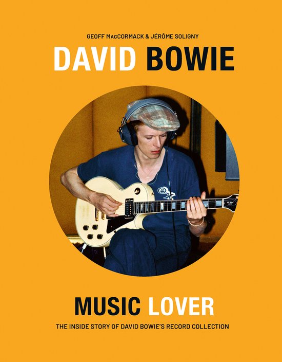 David Bowie met koptelefoon en pet, spelend op een witte gitaar in een studio.