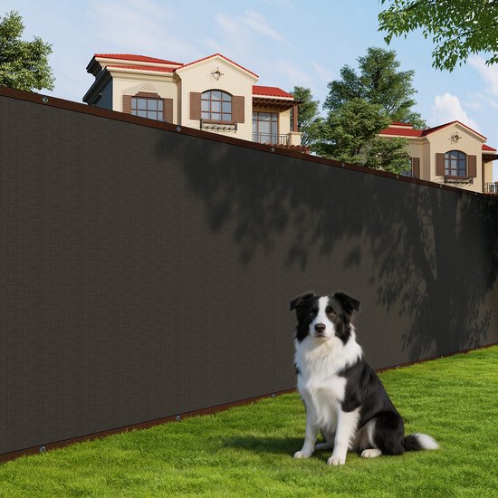 Zwart privacyscherm op een groen gazon voor een huis, met een zittende Border Collie.