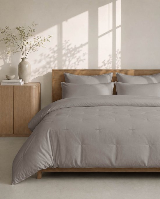 Taupe dekbed opgemaakt op een bed met houten hoofdbord, met geborduurde stiksels.