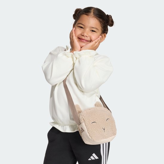 Meisje met een beige teddy tasje in de vorm van een schaapje, draagt een witte trui en zwarte broek.