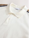 Crème poloshirt met kraag en knoopsluiting. Strepen op de schouder en mouwen zijn zichtbaar.
