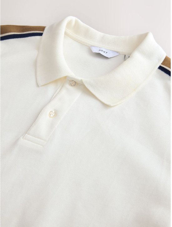 Crème poloshirt met kraag en knoopsluiting. Strepen op de schouder en mouwen zijn zichtbaar.