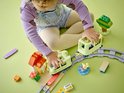 Un jeune enfant en pull violet et salopette joue avec un train vert clair et des rails.