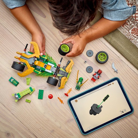 Een jongen bouwt de LEGO Ninjago racewagen (71828) met onderdelen verspreid op de grond, inclusief een tablet met instructies.