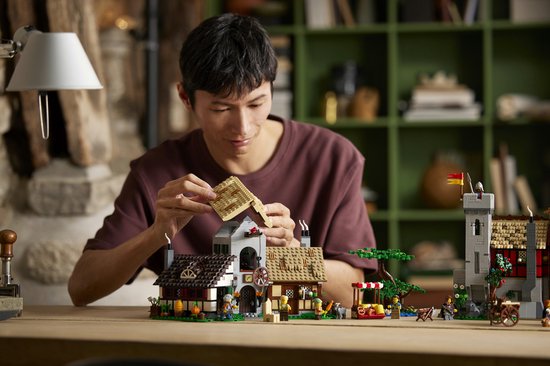 Man bouwt aan de LEGO Icons Middeleeuws stadsplein set, met de boerderij en molen op de voorgrond.