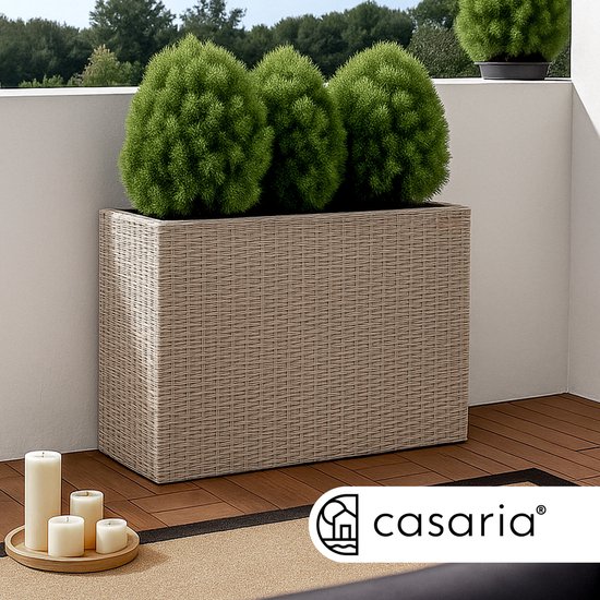 Beige plantenbak met vlechtstructuur op een houten terras, met groene struiken en kaarsen.