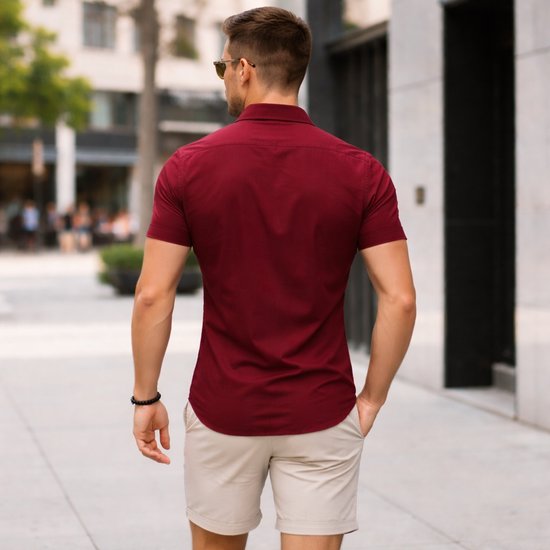 Achterkant van een man in een bordeauxrood overhemd met korte mouwen en beige short. Handen in de zakken.