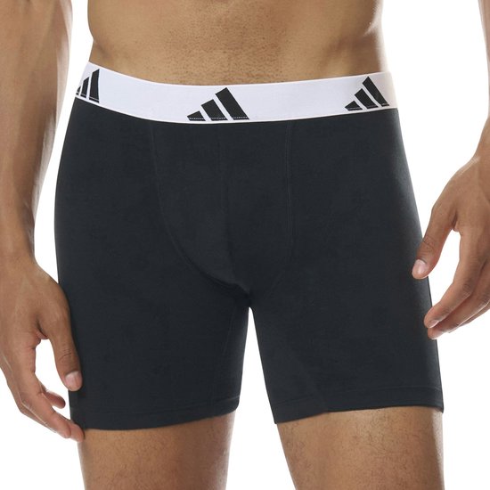 Model draagt zwarte boxershort met witte adidas tailleband.