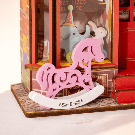 Roze houten hobbelpaardje met sierlijke uitsnijdingen, op een witte ondergrond, voor een miniatuur speelgoedwinkel.