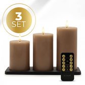 Set van drie bruine LED-kaarsen op een zwarte standaard, met een afstandsbediening ervoor. De kaarsen hebben een nepvlam en gloeien.