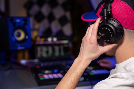 Jonge man met pet en zwarte koptelefoon, DJ-apparatuur op de achtergrond.