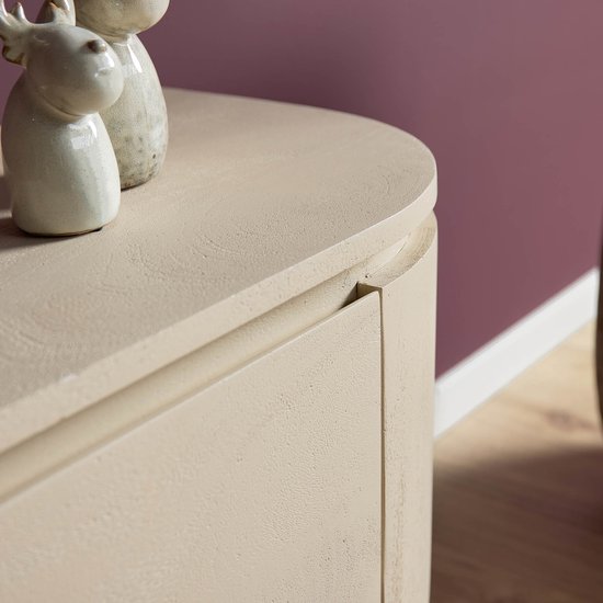 Zandkleurig houten tv-meubel met afgeronde hoeken en decoraties bovenop, op een paarse muur.