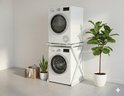 Wit wasmachine-opbouwmeubel met een droger erop. Naast een plant en een mandje.