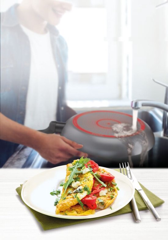 Omelet met tomaat en rucola op een bord, met een pan die wordt afgespoeld in de gootsteen.