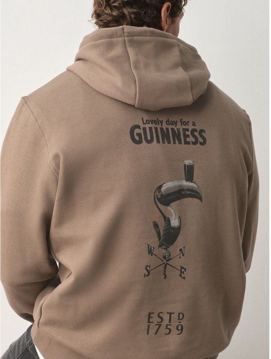 Achterkant bruine hoodie met tekst 'Lovely day for a GUINNESS' en een afbeelding van een toekan met een glas Guinness.