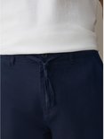 Detailopname van de taille met knoopsluiting en trekkoord op de donkerblauwe broek.