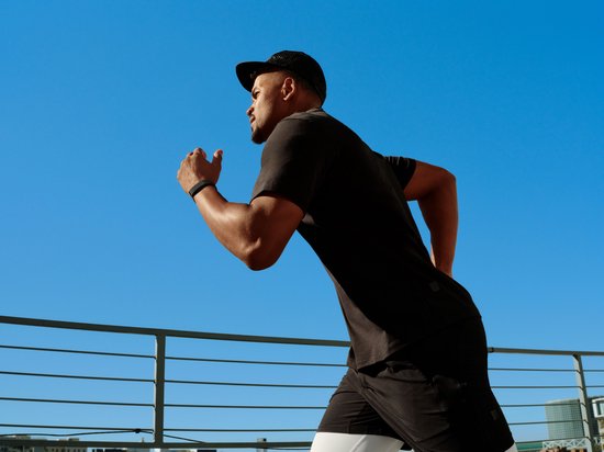 Man met zwarte pet en sportkleding draagt een donkergrijs bandje om zijn linkerpols tijdens het hardlopen.
