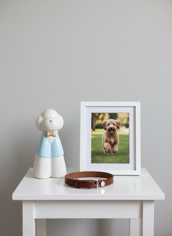 Witte keramieken hond met lichtblauwe jas en gouden strik, naast een fotolijst met hond.