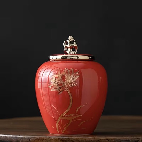 Rode keramische urn met gouden lotusbloem-decoratie en glanzende deksel.