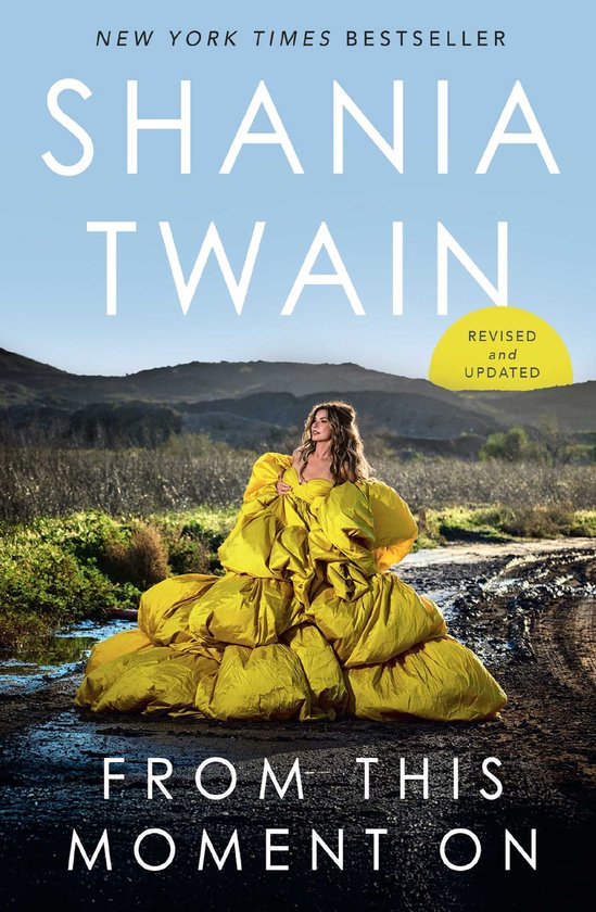 Boek 'From This Moment On' van Shania Twain met op de cover een vrouw in een gele jurk in een landschap.