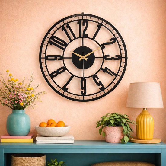 Zwarte industriële wandklok met Romeinse cijfers en gouden wijzers, boven een dressoir met decoraties.