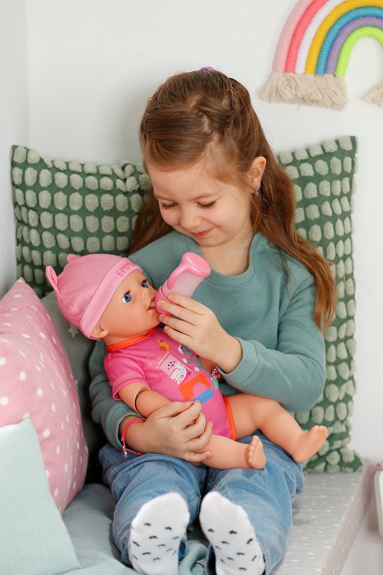 Kindje voedt BABY born Emma pop met flesje. Pop draagt roze outfit en muts met oortjes.