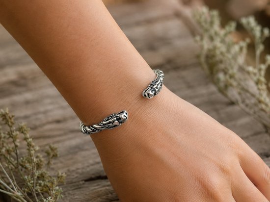 Zilverkleurige, gedraaide armband met drakenkopuiteinden gedragen op een pols.