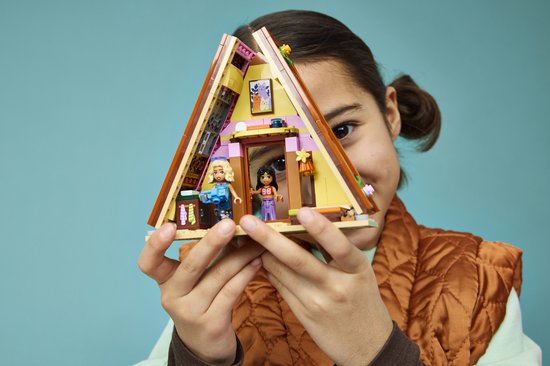 Kind houdt een Lego Friends speelgoedhuisje met roze accenten vast.