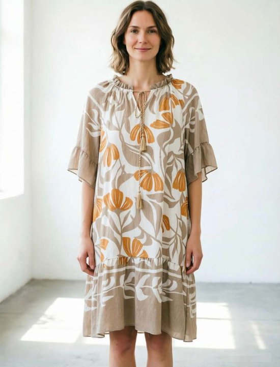 Een beige zomerjurk met een bruin-witte bloemenprint. De jurk heeft ruches aan de halslijn, driekwartmouwen en een volant aan de zoom.