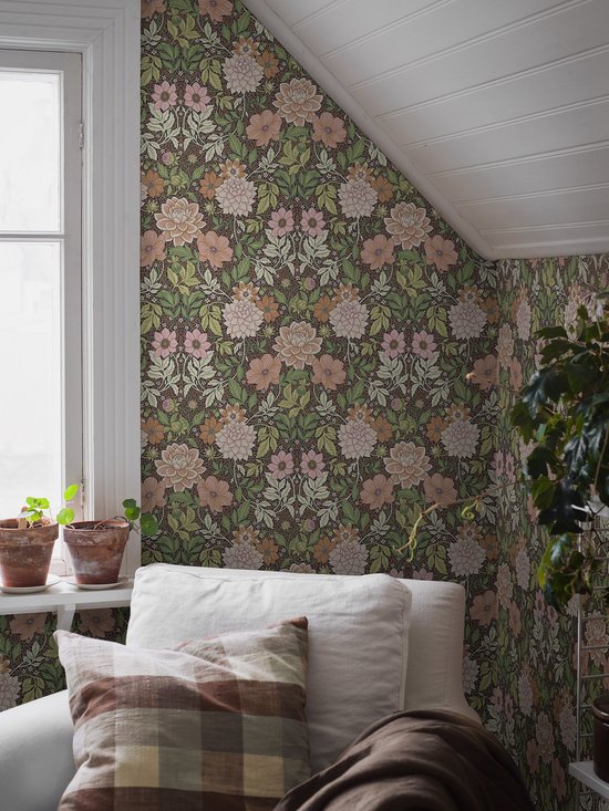 Een woonkamer met behang in een groen en roze bloemenpatroon. Een witte bank staat voor de behangen muur.