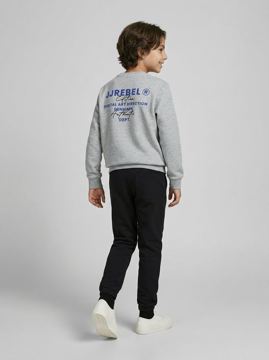 Jongen van achteren gezien, draagt een grijze sweater met blauwe opdruk en een zwarte joggingbroek.